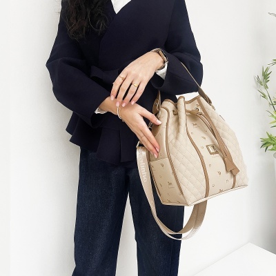 Saco de mão bege acolchoado com padrão castanho e alça larga, em uso