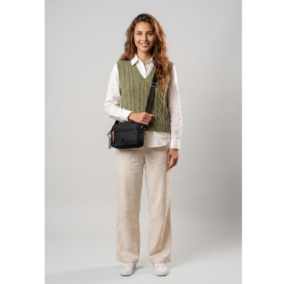 Mulher com colete verde, camisa branca, calças bege, sapatos brancos e bolsa preta