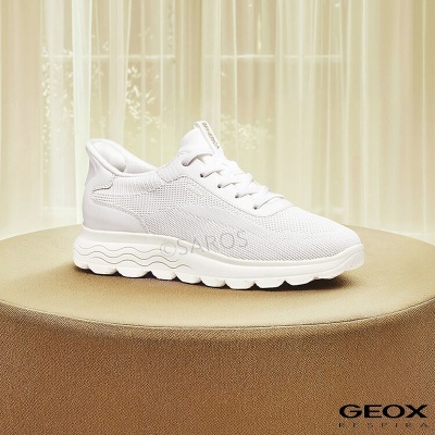 Ténis branco Geox Respira em malha com sola ondulada sobre superfície dourada e cortinado bege