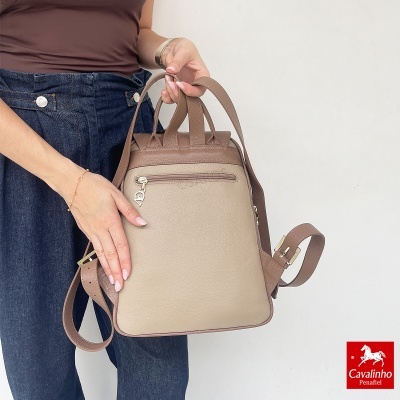Mochila bege e castanha de pele sintética com fecho zip e alças, a ser segurada por uma pessoa
