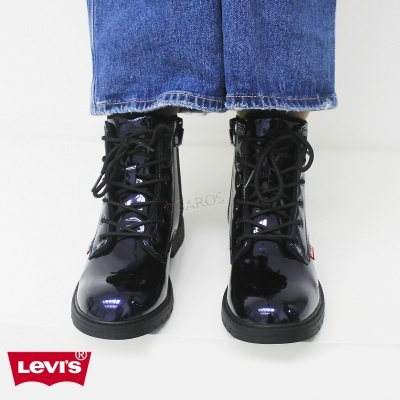 Botas pretas de verniz com atacadores pretos e sola preta, usadas com calças de ganga azul