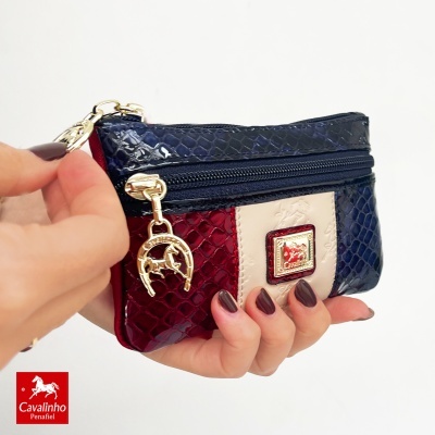 Carteira pequena tricolor com textura de pele de cobra e pendente dourado.