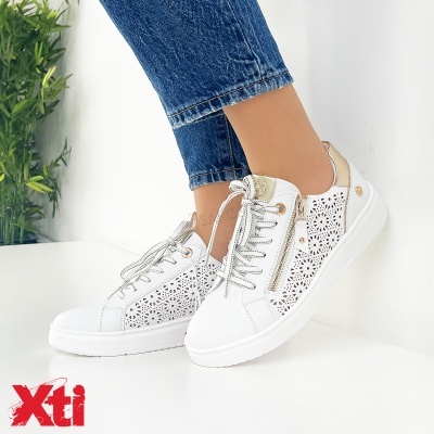 Tênis brancos com detalhes dourados e padrão floral perfurado usados por mulher