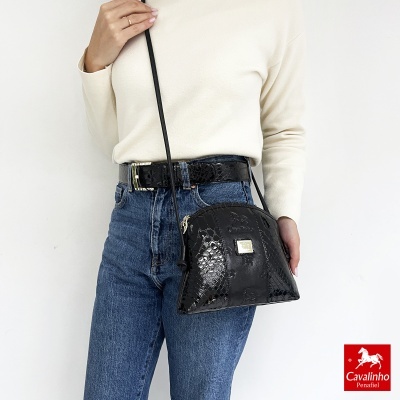 Mala preta com textura de pele de crocodilo, alça longa, usada com camisola creme e jeans azuis.