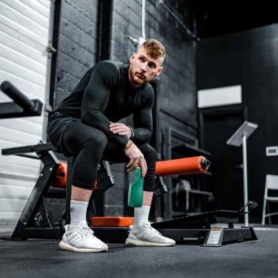 Homem sentado numa academia com roupa desportiva preta a segurar garrafa verde