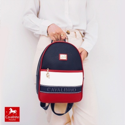Mochila tricolor Cavalinho com logótipo, em mão de pessoa com camisa branca e calças claras.