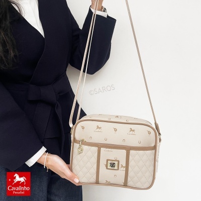 Mala de ombro bege com padrões Cavalinho e fecho dourado, exibida com casaco preto
