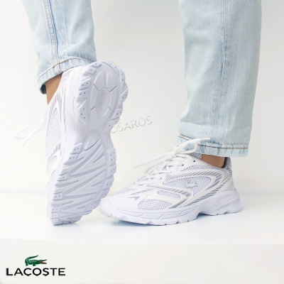 Ténis desportivos brancos Lacoste com sola antiderrapante e malha respirável, usados com calças de ganga claras