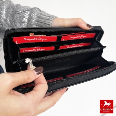 Carteira preta texturizada com bolsos para cartões vermelhos 'Designed to fit you.', sendo segurada por mãos com unhas pintadas.
