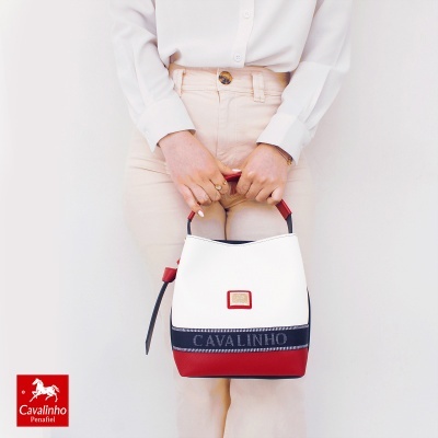 Bolsa de mão Cavalinho branca, vermelha e azul escuro com detalhes em pessoa com camisa branca e calças bege