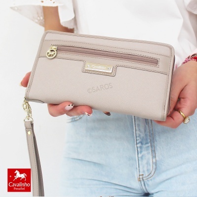 Carteira feminina bege com zíper e placa metálica Cavalinho, segurada por pessoa com camisa branca e jeans