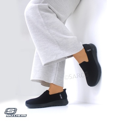 Sapatilhas Skechers pretas em tecido com sola preta, calça cinza claro em fundo branco.
