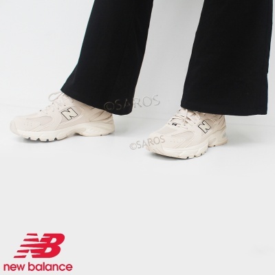 Ténis New Balance bege claro com logo N preto e sola branca, calças pretas