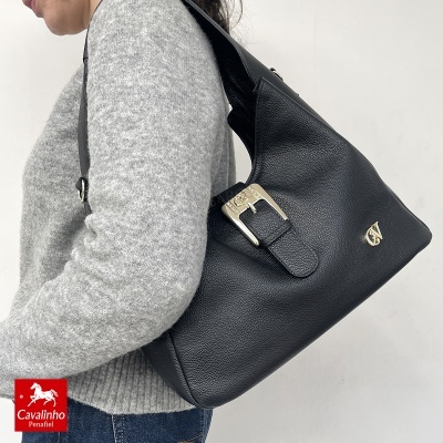 Mala preta em pele com fivela dourada e logótipo Cavalinho Penafiel usada ao ombro