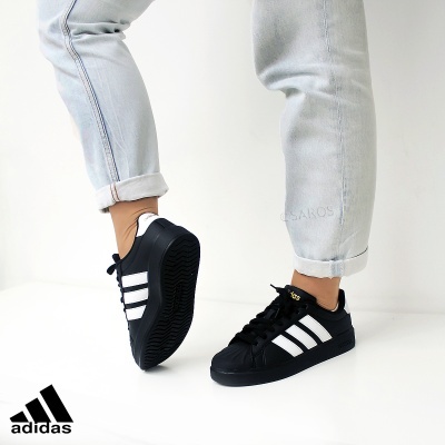 Ténis Adidas pretos com riscas brancas usados em fundo branco