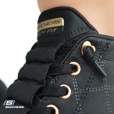 Tênis preto Skechers com ilhós dourados e etiqueta na língua.