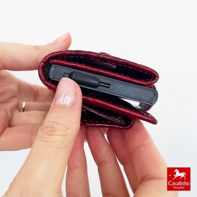 Carteira vermelha de pele a segurar telemóvel preto nas mãos femininas