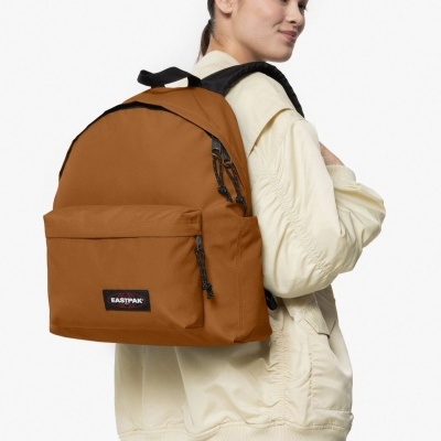 Mochila castanha EASTPAK com detalhes pretos usada por pessoa com casaco creme e jeans azuis