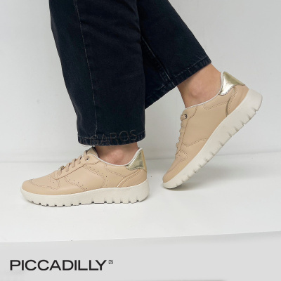 Ténis de senhora bege com detalhe dourado e sola branca, usados com calças pretas sobre fundo branco com texto PICCADILLY