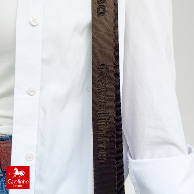Cinto preto de tecido com padrão de texto em relevo ao lado de camisa branca e calças jeans