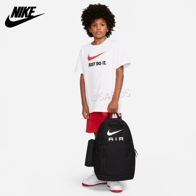 Criança com t-shirt branca Nike 'JUST DO IT.', calções vermelhos e mochila preta Nike Air