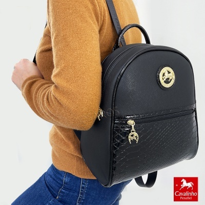 Mochila preta com detalhes dourados e textura tipo pele de cobra usada numa pessoa