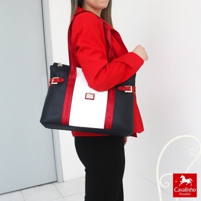 Mala de senhora preta e branca com alças vermelhas e detalhes dourados, usada por mulher com casaco vermelho