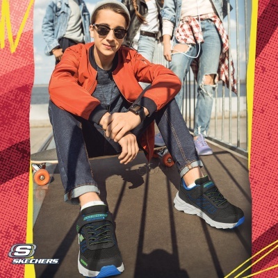 Jovem sentado num skate usando ténis Skechers pretos com detalhes azuis e verdes