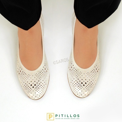 Sapatilhas brancas com recortes usadas com calças pretas sobre fundo branco