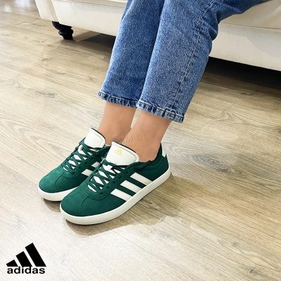Ténis Adidas verdes e brancos em chão de madeira