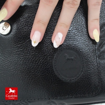 Mão com unhas decoradas sobre mala preta de couro Cavalinho