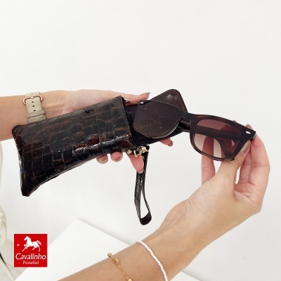 Óculos de sol a ser retirados de estojo de pele castanha com textura de crocodilo