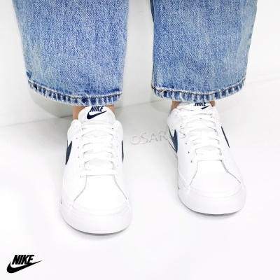 Ténis Nike brancos com logo azul escuro usados com jeans azuis sobre fundo branco