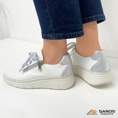 Sapatilhas brancas em couro com parte traseira prateada usadas com jeans azul escuro