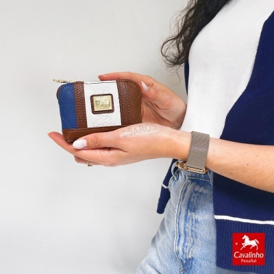 Carteira pequena azul, branca e castanha com logótipo Cavalinho nas mãos de uma pessoa