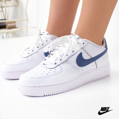 Ténis Nike Air Force 1 brancos com swoosh azul usados numa pessoa