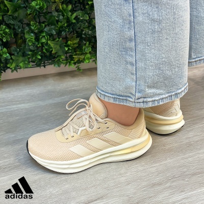 Ténis Adidas bege claro em piso claro com plantas ao fundo