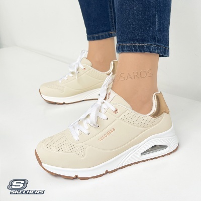 Ténis bege Skechers com detalhes dourados e sola branca, usados com jeans azuis