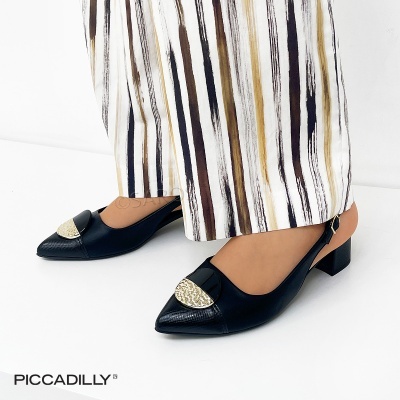 Sapatos pretos com salto baixo e detalhe dourado, usados com calças às riscas.