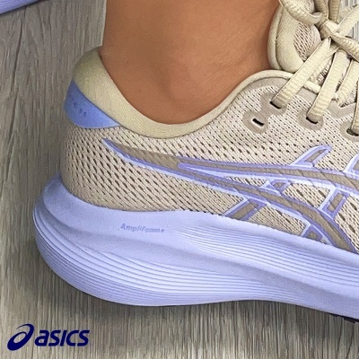Ténis de corrida ASICS bege com detalhes lilás em chão de madeira.