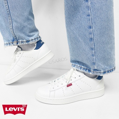 Ténis brancos Levis com detalhe azul e etiqueta vermelha, com calças de ganga