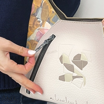 Bolsa bege clara com padrão geométrico e fecho preto em destaque.