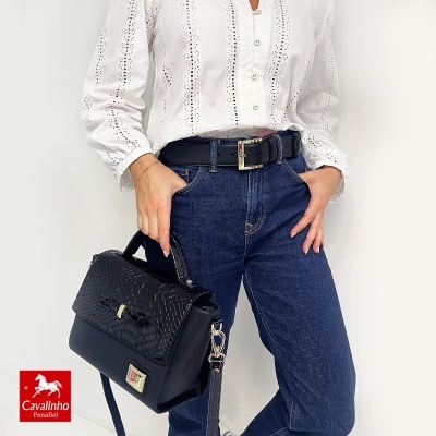 Mala preta padrão crocodilo, cinto preto, jeans e camisa branca bordada