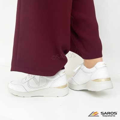Sapatilhas brancas com detalhes dourados e atacadores junto a calças bordô.