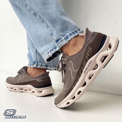 Ténis Skechers castanhos com sola branca e detalhes diversos, usados com jeans azuis