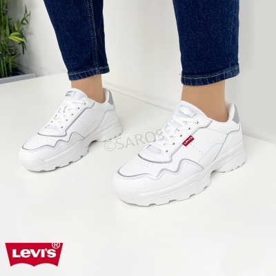 Sapatilhas brancas Levi's com sola grossa e detalhes cinza usadas com jeans.
