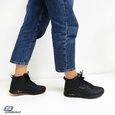 Ténis pretos Skechers com sola castanha usados com jeans azuis.