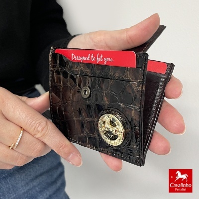 Carteira pequena em pele castanha com padrão croco e botão metálico dourado, cartão vermelho visível.