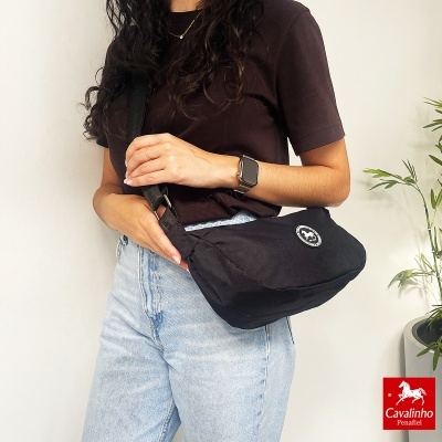 Mulher com mala tiracolo preta, t-shirt castanha e calças de ganga claras.