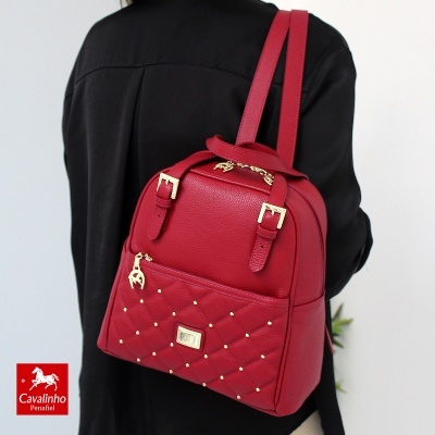 Mochila vermelha Cavalinho Penafiel com detalhes dourados numa pessoa com casaco preto